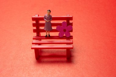 Bir adam ve bir kadının minyatür figürlü sembolik bir fotoğrafla bankta duruşu.