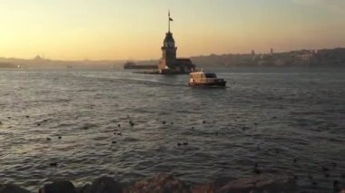 Tarihsel Bakire Kulesi veya Kiz Kulesi ve günbatımında bir eğlence teknesi - İstanbul, Türkiye.