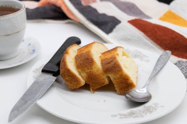 Beyaz arka planda bir tabakta bir fincan çayla birlikte bir dilim kek.