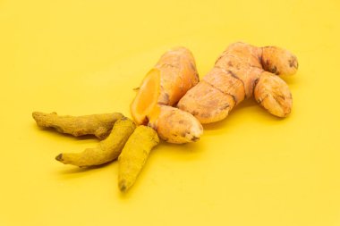 Sarı zemin üzerinde izole edilmiş taze zerdeçal kökü dilimleri
