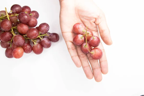 Red grapes in a hand placed on a white background, View from above