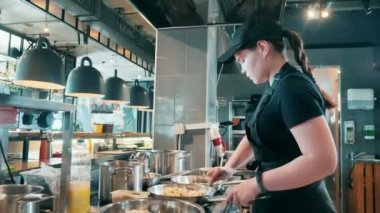 Kadın aşçı çeşitli tavalarda yemek pişiriyor.