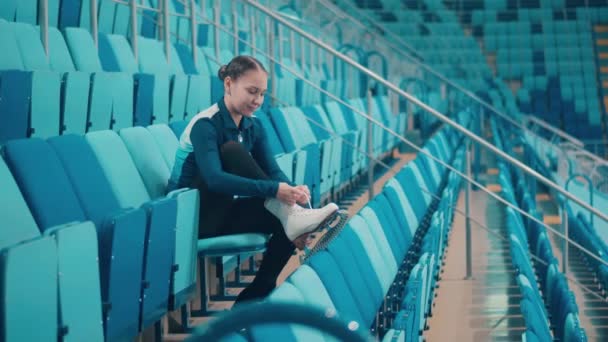 Sportarena mit einem jungen Mädchen, das seine Eislaufschuhe schnürt — Stockvideo