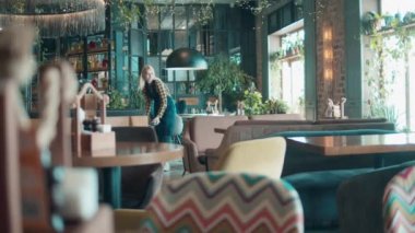 Restoran salonu sarışın bir garson tarafından temizleniyor.