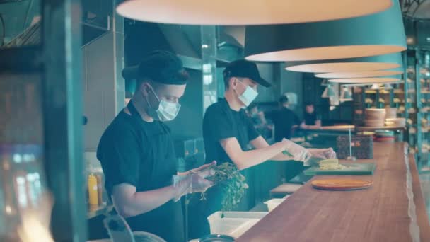 Cooks in face masks are processing ingredients at the counter — Stock Video