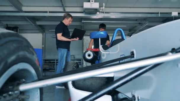 Механики говорят о гоночной машине в гараже — стоковое видео