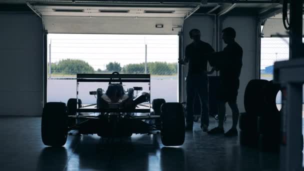 Coche de carreras aparcado dentro de un garaje con dos mecánicos — Vídeo de stock