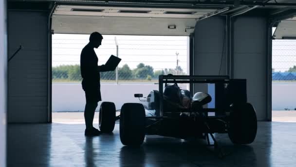 Um mecânico com um laptop está verificando um carro de corrida — Vídeo de Stock