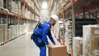 Depo çalışanı ergoskeleton giyiyor ve bir kutu kaldırıyor.