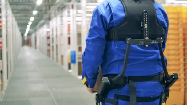 Mitarbeiter trägt Ergoskelett und läuft durch das Lager — Stockvideo