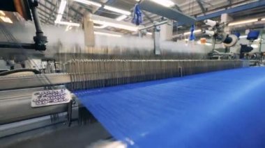 Dokuma mekanizması renkli ipliklerden kumaş üretiyor.