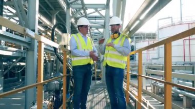 İki müfettiş petrol rafinerisi hakkında tartışıyorlar.