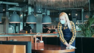 Yüz maskesi takan bayan garson restoranda temizlik yapıyor. Covid-19 sırasında küçük işletmeler, koronavirüs salgını.