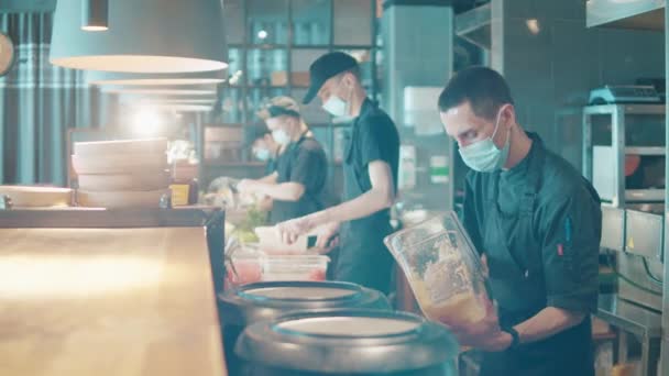 I membri del personale della cucina con maschere facciali stanno lavorando al bancone. Piccola impresa durante la covid-19, pandemia di coronavirus. — Video Stock