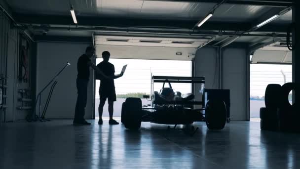 Δύο επαγγελματίες κοιτάζουν το αγωνιστικό αυτοκίνητο στο εργαστήριο. — Αρχείο Βίντεο