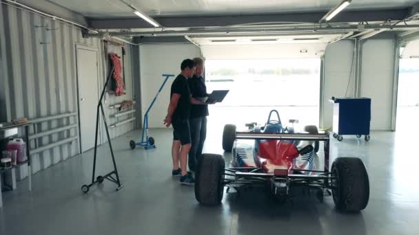 Taller con dos especialistas hablando de su coche de carreras — Vídeos de Stock