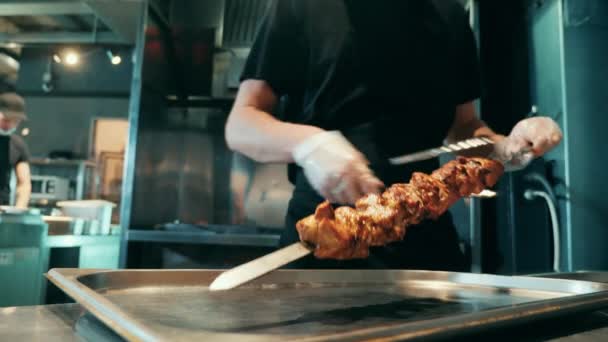 Un cocinero está sacando carne asada del pincho. — Vídeo de stock