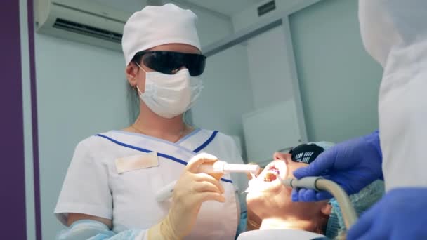 Стоматологи освещают зубы пациентов во время отбеливания — стоковое видео