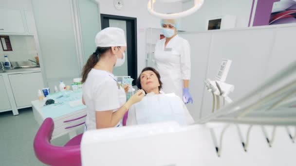 Paciente femenina está hablando con dentistas mientras está en una silla — Vídeo de stock