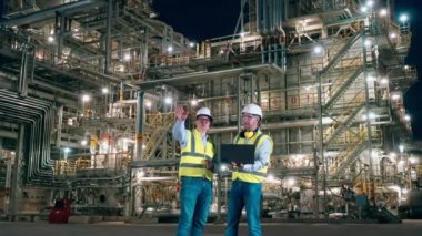 İki iş arkadaşı gece petrol işleme fabrikasında konuşuyorlar.