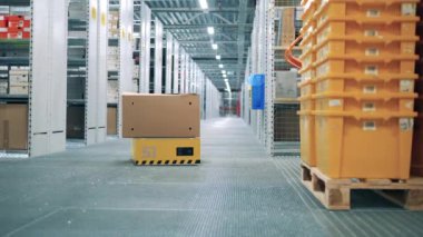 Bir robot sırtında bir paketle depodan geçiyor.