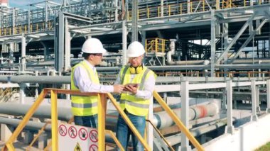 Fabrikadaki modern endüstriyel işçiler. Petrol rafinerisi çalışanları dışarıda sohbet ediyorlar.