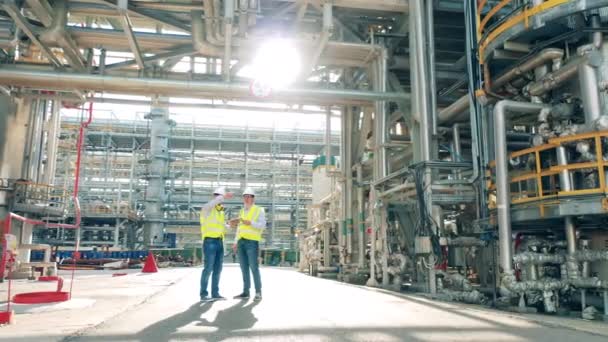 Raffinaderimedarbetare diskuterar konstruktioner av fabriken. Moderna industriarbetare vid fabriksanläggningen. — Stockvideo