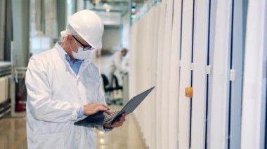 Fabrika işçisi dizüstü bilgisayarda yazarken ekipmanları gözlemliyor