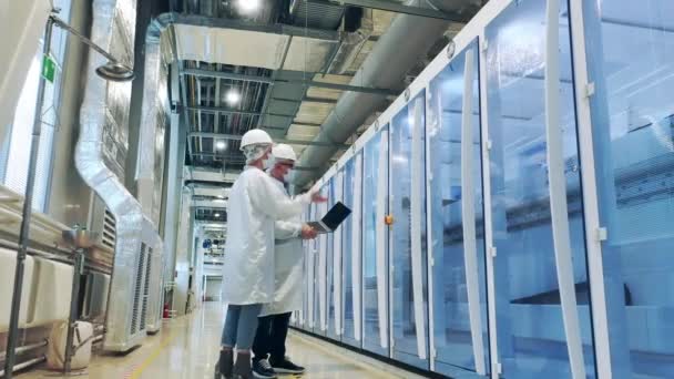 Завод солнечных батарей с двумя рабочими, наблюдающими за работой машин — стоковое видео
