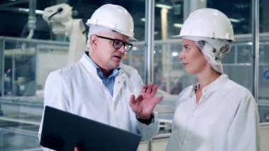 Mühendisler, ekip çalışması, modern fabrika tesisi. Güneş pili fabrikasında laboratuvar önlüğü uzmanı iki kişi konuşuyor.