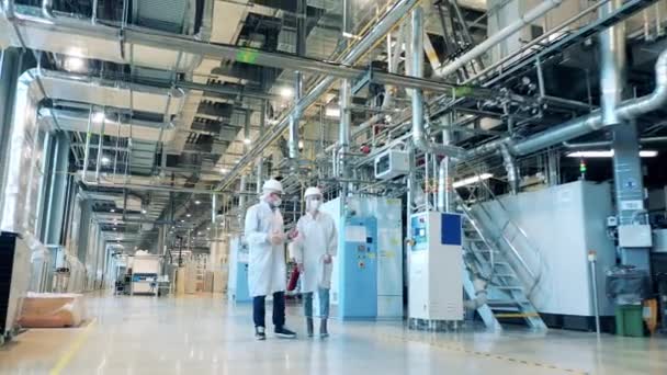 Factory facility, engineers working at a modern industrial plant. Modern factory unit with two specialists walking along it — Stock Video