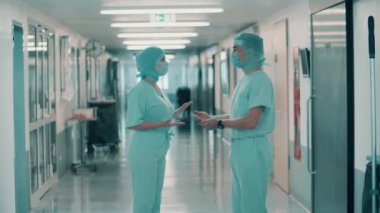 Cerrahi üniformalı iki doktor koridorda konuşuyor.