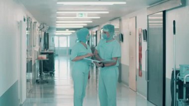 Cerrahi üniformalı iki doktor koridorda konuşuyor.