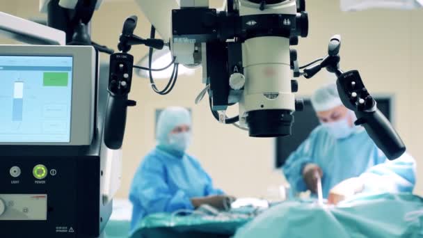 Dispositivo microscópico con cirujanos operando a un paciente al lado — Vídeo de stock