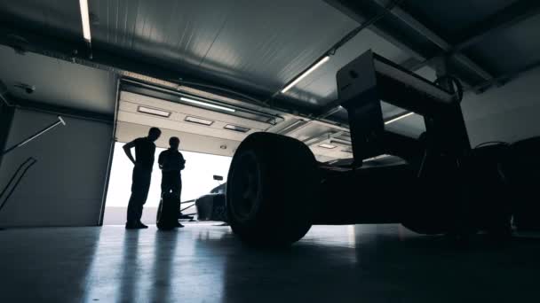 За спортивным автомобилем наблюдают два гонщика в гараже — стоковое видео