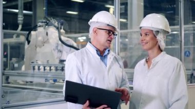 İki mühendis robotik makinelerin yanında konuşuyor.