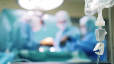 Ameliyat sürecinin bulanık görüntüsü ve yanında bir serum torbası asılı.