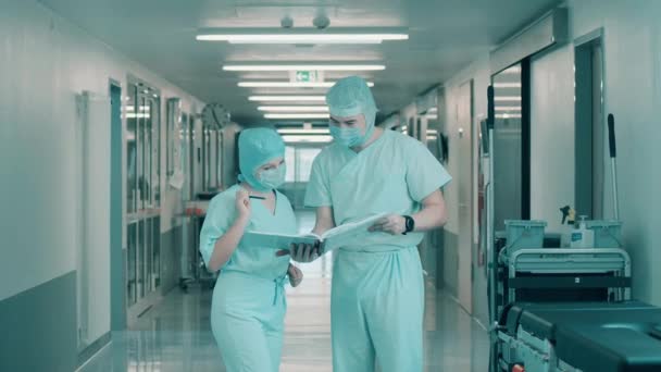 Два врача в хирургической форме просматривают медицинские записи — стоковое видео