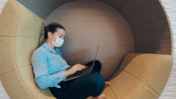 Uma mulher está usando uma máscara facial e trabalhando em seu laptop — Vídeo de Stock