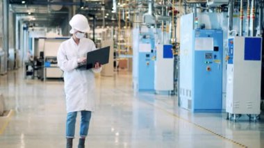 Yüz maskesi takan kadın çalışan fabrikayı gözetliyor.