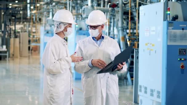 Dos empleados de fábrica con máscaras faciales están observando las instalaciones — Vídeos de Stock