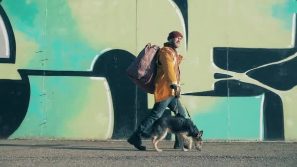 Бродяга идет по улице с собакой и огромной сумкой — стоковое видео
