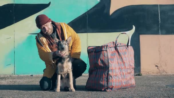 Ein Landstreicher streichelt seinen Hund mit einer dicken Tüte neben sich — Stockvideo