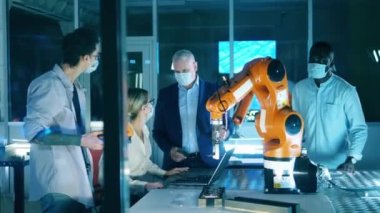 Yüz maskeli bilişim mühendisleri robotları tartışıyor.