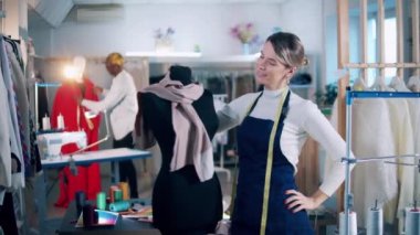A seamstress is smiling while standing next to a dummy