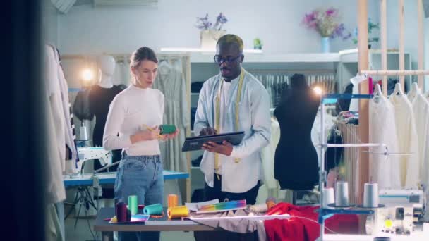 African tailor is showing tools to a seamstress in the workshop — Vídeo de Stock