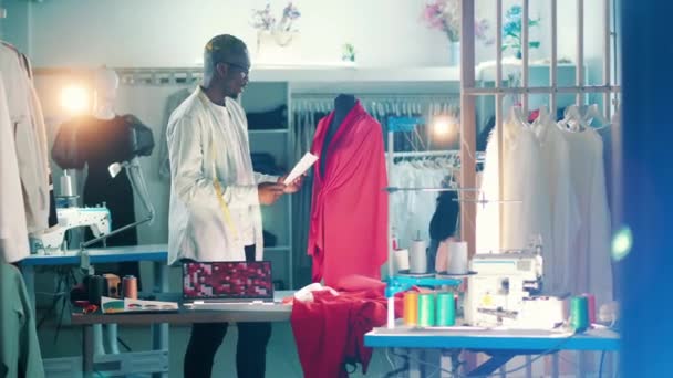 African tailor is looking at a dress and its sketch — Vídeo de Stock