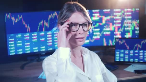 Female stockbroker and monitors with stock data behind her — Vídeo de stock