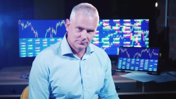 Male stockbroker is sitting next to computers and smiling — Stock Video