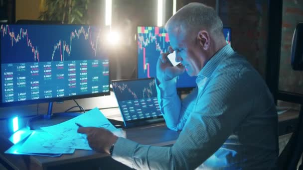 A stockbroker is talking on the phone while monitoring the data — Vídeo de stock